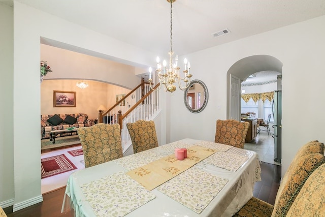 dining room featuring a notable chandelier, arched walkways, stairs, visible vents, and dark wood-style floors