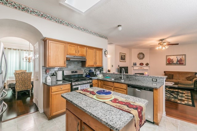 kitchen featuring appliances with stainless steel finishes, a sink, a peninsula, open floor plan, and under cabinet range hood