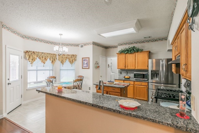 kitchen featuring a textured ceiling, a chandelier, dark stone countertops, stainless steel appliances, and a peninsula