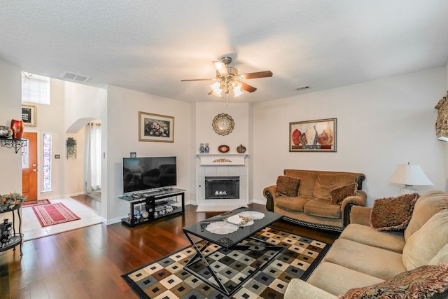 living area with visible vents, a ceiling fan, wood finished floors, a tiled fireplace, and arched walkways
