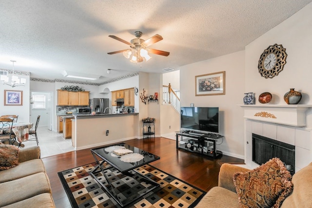 living area with stairs, a textured ceiling, ceiling fan with notable chandelier, and wood finished floors