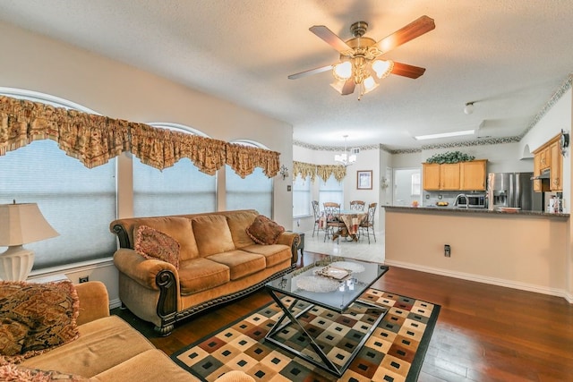 living area with baseboards, ceiling fan with notable chandelier, a textured ceiling, and dark wood-type flooring