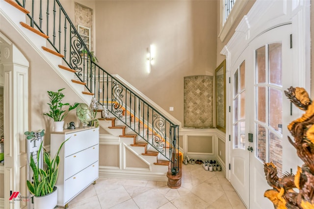 foyer with a decorative wall, stairs, a wainscoted wall, and a towering ceiling