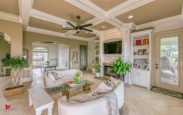 living area featuring crown molding, ceiling fan, arched walkways, a high end fireplace, and coffered ceiling