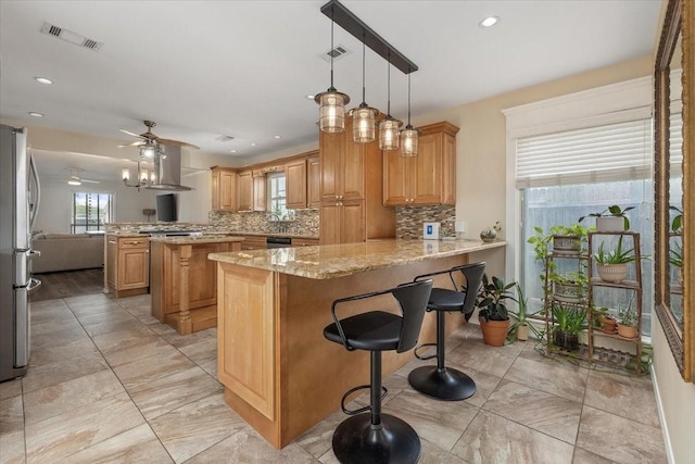 kitchen featuring visible vents, a peninsula, wall chimney range hood, backsplash, and stainless steel appliances