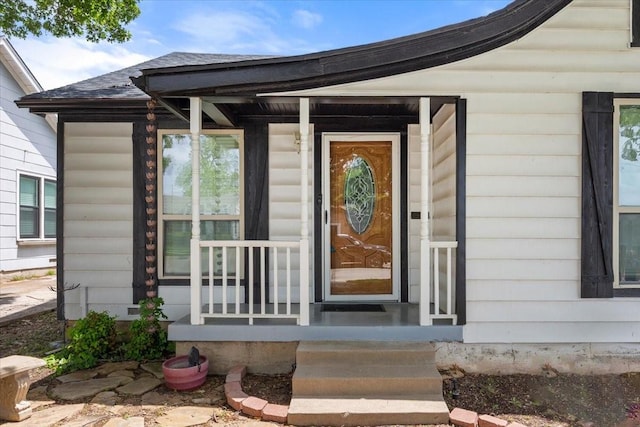 view of exterior entry featuring covered porch and a shingled roof