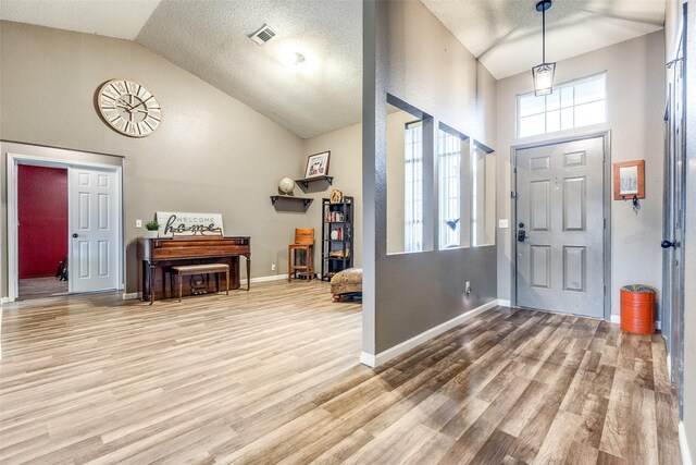 foyer with visible vents, baseboards, high vaulted ceiling, a textured ceiling, and light wood-style flooring