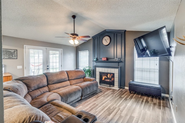 living area featuring wood finished floors, a textured ceiling, a tiled fireplace, a ceiling fan, and vaulted ceiling