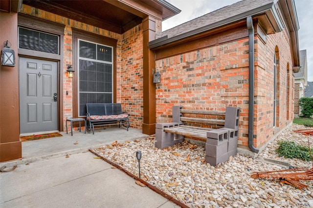 view of exterior entry featuring a porch, brick siding, and roof with shingles