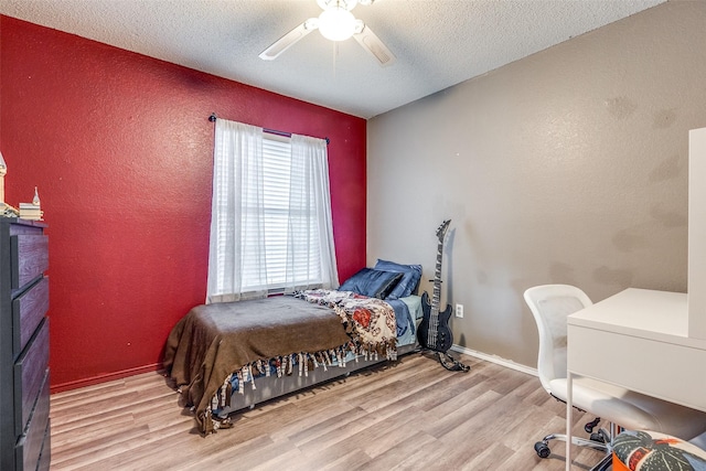 bedroom with light wood-type flooring, a textured ceiling, ceiling fan, and a textured wall