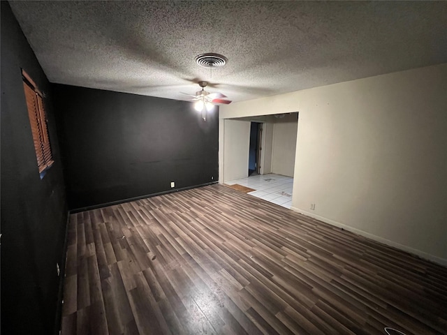 empty room with ceiling fan, a textured ceiling, visible vents, wood finished floors, and baseboards