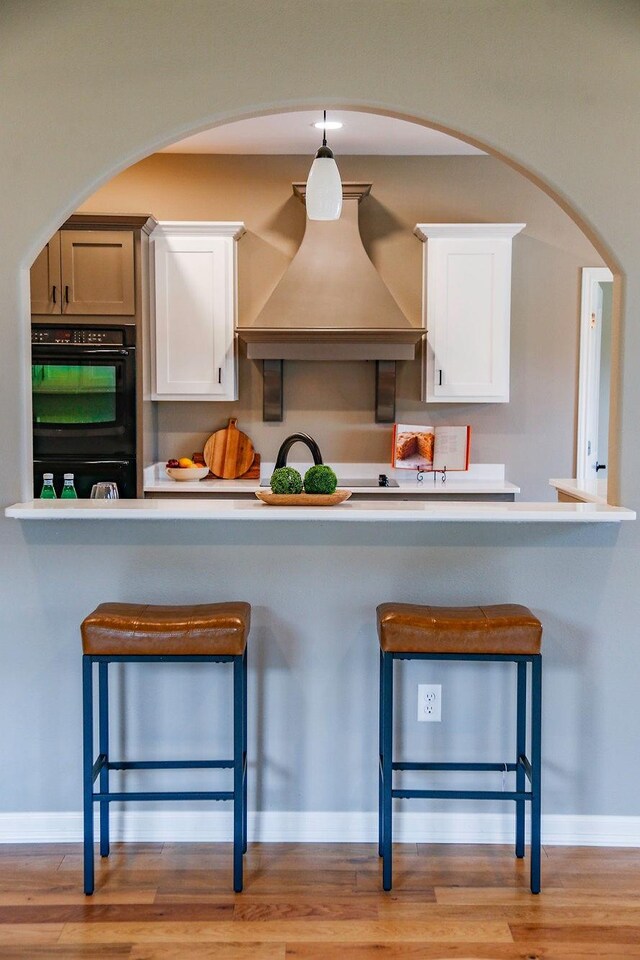 kitchen with light countertops, dobule oven black, custom exhaust hood, and white cabinetry