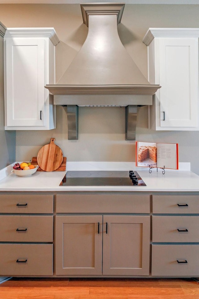 kitchen featuring light countertops, premium range hood, light wood-style flooring, and black electric cooktop