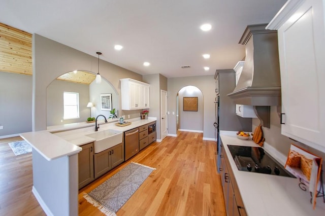 kitchen featuring appliances with stainless steel finishes, a sink, arched walkways, premium range hood, and a peninsula