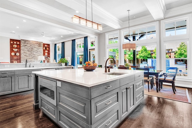 kitchen with dark wood-style flooring, an island with sink, gray cabinets, stainless steel microwave, and a sink