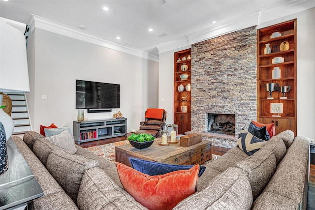 living room with a stone fireplace, built in shelves, wood finished floors, ornamental molding, and recessed lighting