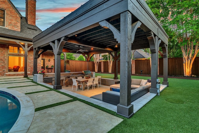 patio terrace at dusk with a gazebo, a fenced backyard, a yard, and an outdoor kitchen