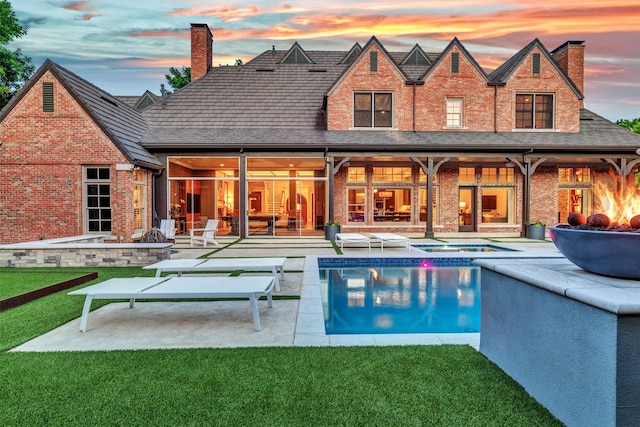 back of house at dusk featuring an in ground hot tub, a patio, a chimney, and brick siding