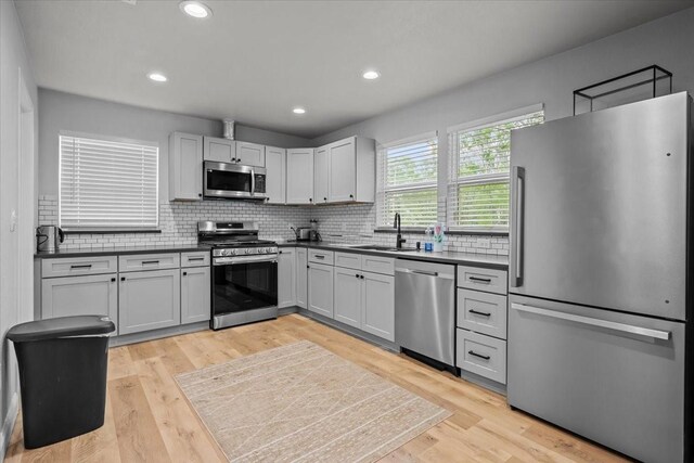 kitchen with dark countertops, appliances with stainless steel finishes, a sink, light wood-style floors, and tasteful backsplash