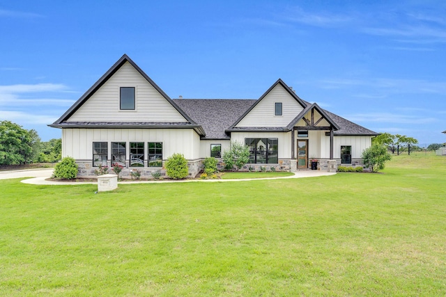 modern farmhouse style home featuring roof with shingles, board and batten siding, a front lawn, and stone siding