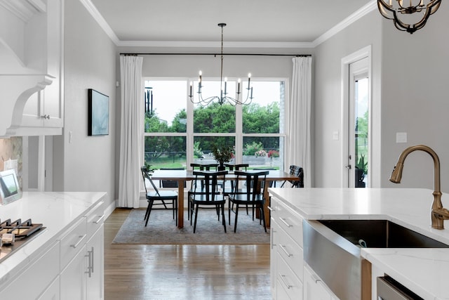 kitchen with light stone counters, a sink, light wood-style floors, a chandelier, and ornamental molding