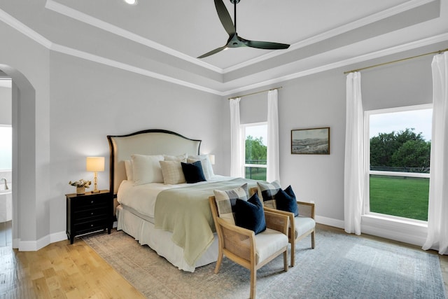 bedroom featuring a raised ceiling, arched walkways, light wood-style flooring, baseboards, and ornamental molding