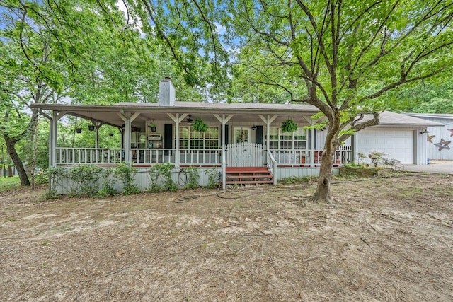 view of front facade with a porch, driveway, a chimney, and a garage