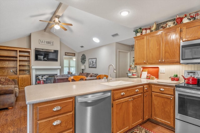 kitchen with a sink, light wood finished floors, stainless steel appliances, open floor plan, and a peninsula