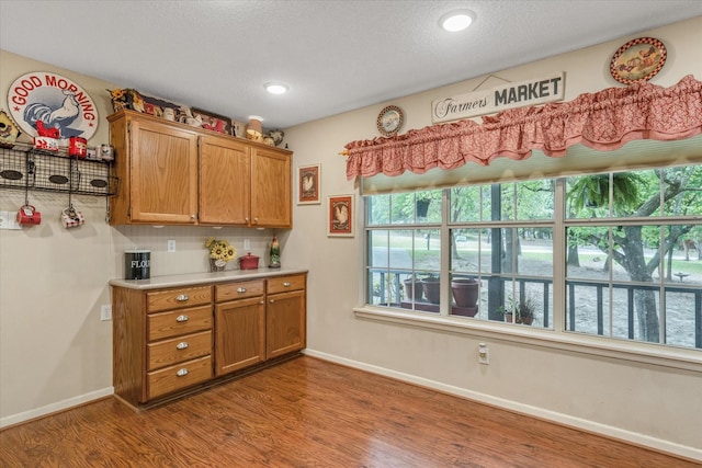 kitchen with dark wood-type flooring, light countertops, baseboards, and brown cabinets