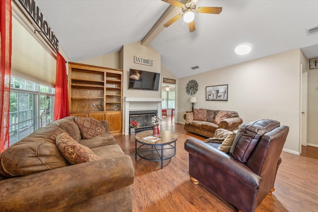 living room featuring a glass covered fireplace, a ceiling fan, baseboards, vaulted ceiling with beams, and wood finished floors