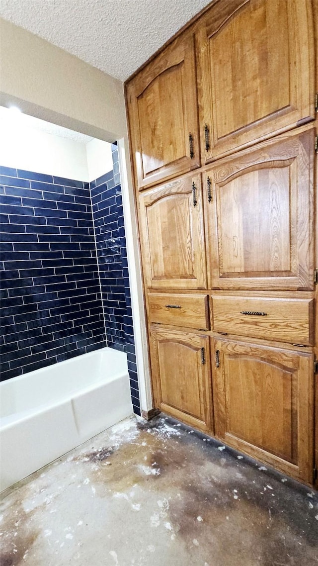 bathroom with a textured ceiling, concrete flooring, and shower / bathing tub combination