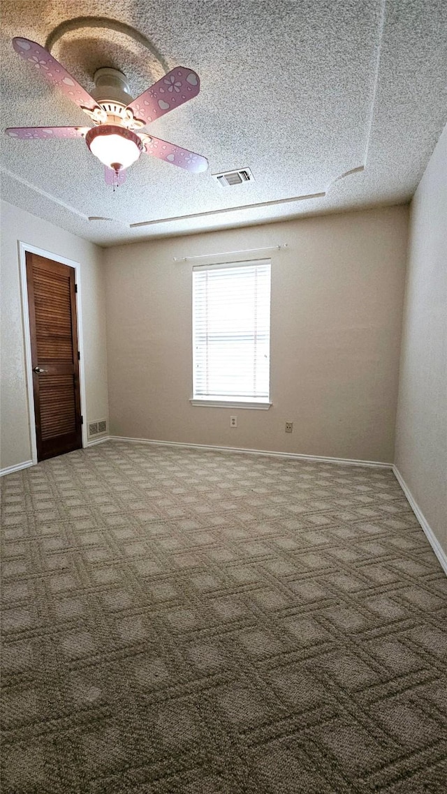 carpeted spare room featuring visible vents, a ceiling fan, and a textured ceiling