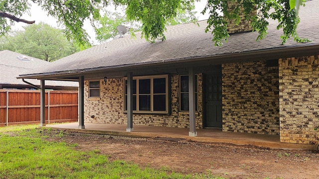 back of property featuring a patio, roof with shingles, fence, and stone siding