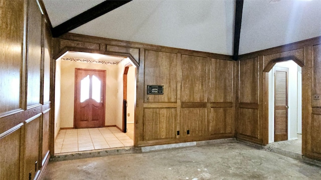 foyer featuring concrete flooring, lofted ceiling with beams, a decorative wall, arched walkways, and wood walls