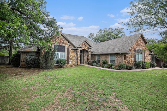 view of front of house featuring roof with shingles, fence, a front yard, and stone siding