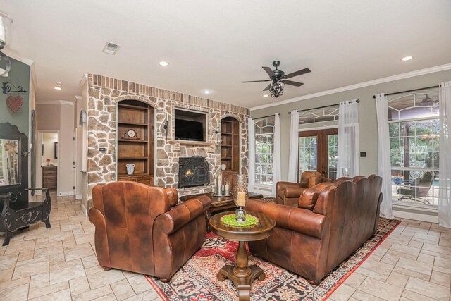 living room featuring crown molding, stone tile flooring, a fireplace, built in shelves, and a ceiling fan