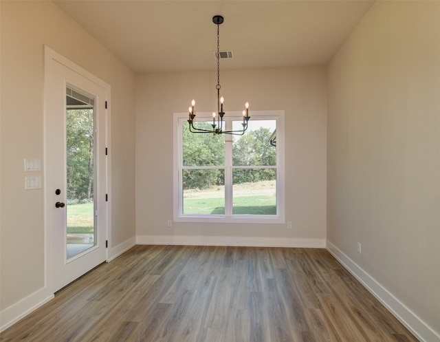 unfurnished dining area featuring baseboards, a notable chandelier, plenty of natural light, and wood finished floors