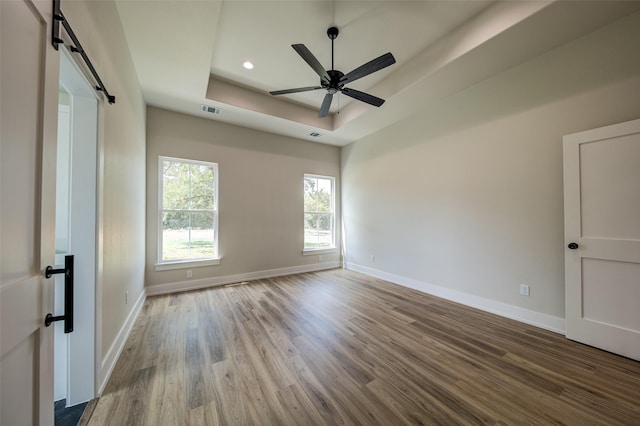 unfurnished room featuring baseboards, visible vents, a barn door, and a raised ceiling
