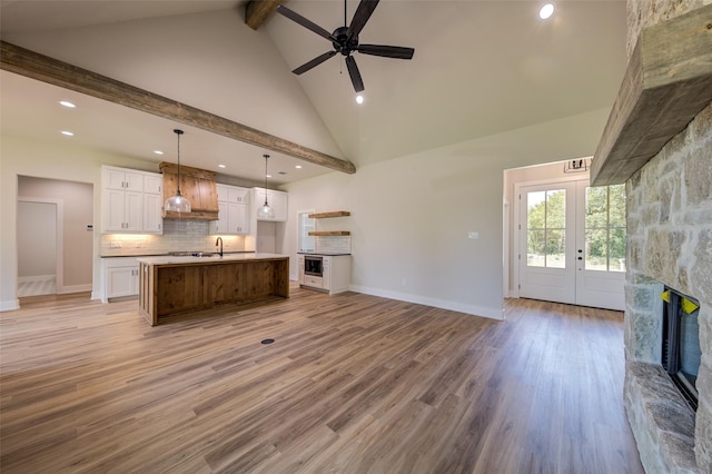 unfurnished living room with light wood finished floors, a stone fireplace, a ceiling fan, recessed lighting, and beamed ceiling