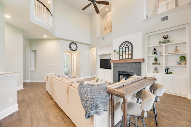 1355 Crockett Dr, Frisco, TX 75033 - living room featuring a brick fireplace, ceiling fan, light wood-style flooring, a towering ceiling, and baseboards