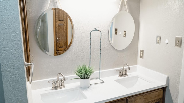 full bath with double vanity, a sink, and a textured wall