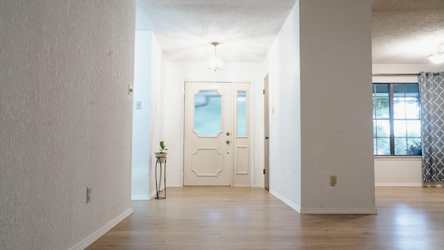 hallway featuring a textured wall, a textured ceiling, a chandelier, baseboards, and wood finished floors