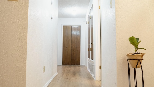 hallway with a textured wall, baseboards, and light wood finished floors