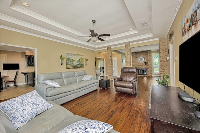 living area with ornamental molding, decorative columns, wood finished floors, ceiling fan, and a raised ceiling
