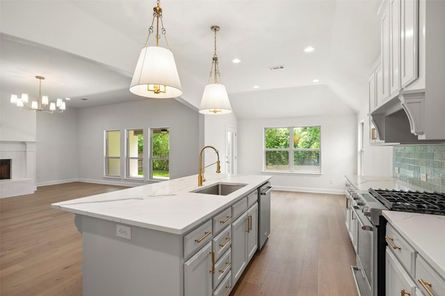 kitchen with visible vents, wood finished floors, a fireplace with raised hearth, a sink, and stainless steel appliances