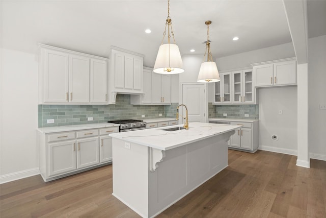kitchen with a sink, decorative backsplash, white cabinetry, and an island with sink