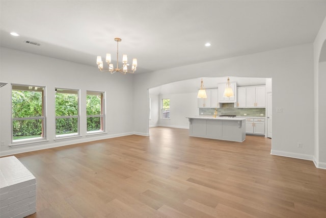 unfurnished living room featuring arched walkways, a chandelier, visible vents, and light wood-style flooring