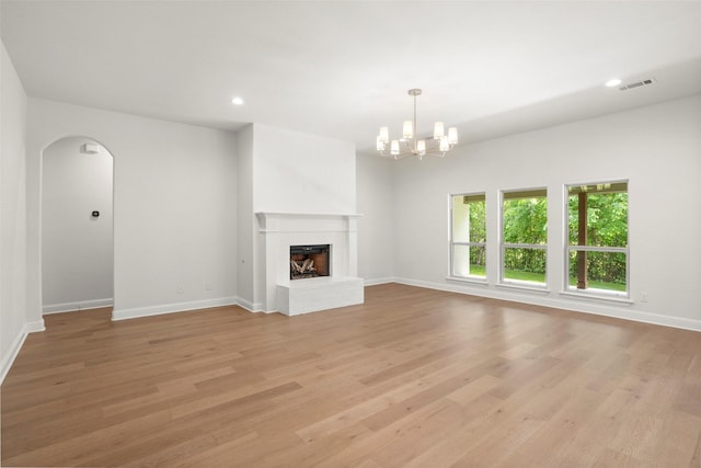 unfurnished living room featuring visible vents, arched walkways, baseboards, light wood finished floors, and an inviting chandelier