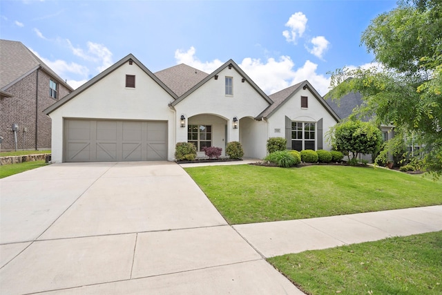 french country inspired facade featuring an attached garage, a front lawn, and concrete driveway