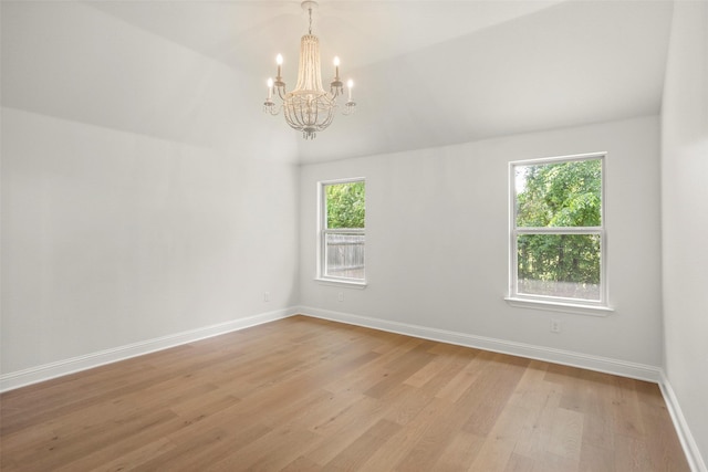 spare room with baseboards, a notable chandelier, plenty of natural light, and light wood finished floors